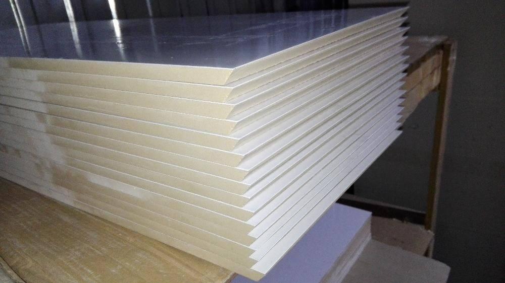 Stos białych, błyszczących płyt z widoczną warstwą izolacyjną na drewnianym regale.