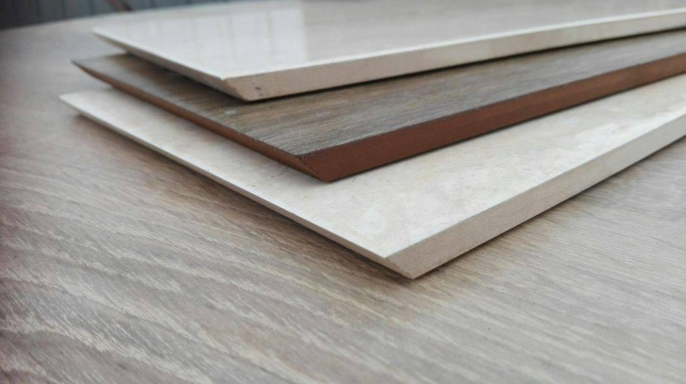 Trzy ułożone na sobie płytki ceramiczne: beżowa polerowana, brązowa imitująca drewno i beżowa matowa, prezentowane na drewnopodobnym blacie.