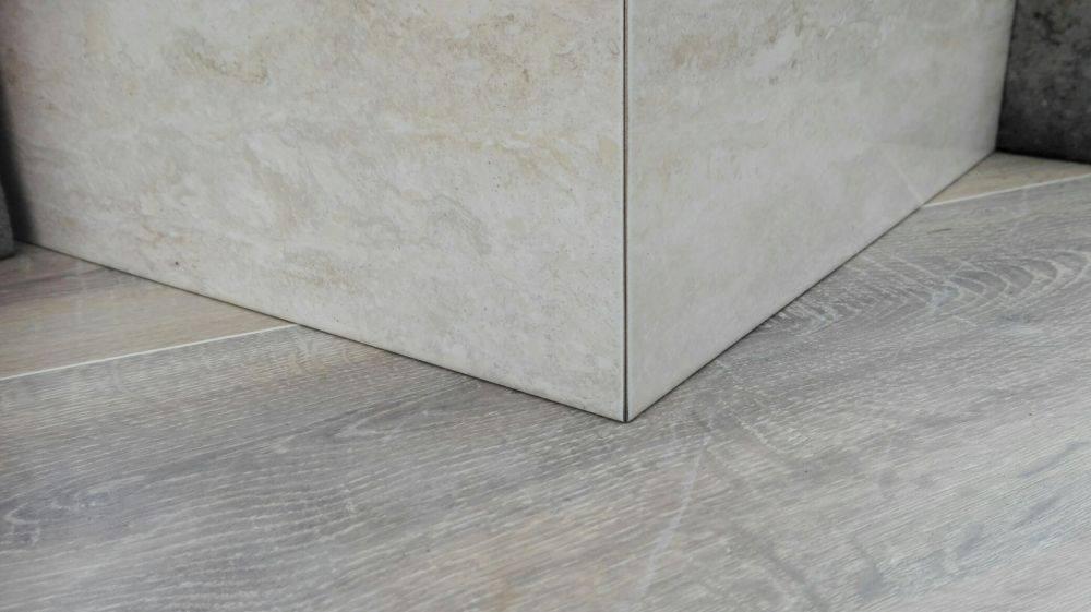 Połączenie jasnych, beżowych płytek imitujących kamień na ścianie z szarą podłogą imitującą drewno, widoczne perfekcyjne spasowanie i fugi.