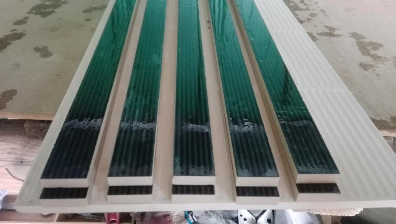 Przygotowane do montażu paski mozaiki szklanej w odcieniach zieleni i czerni, ułożone na podkładzie z białej, karbowanej płyty, z widocznymi śladami kleju