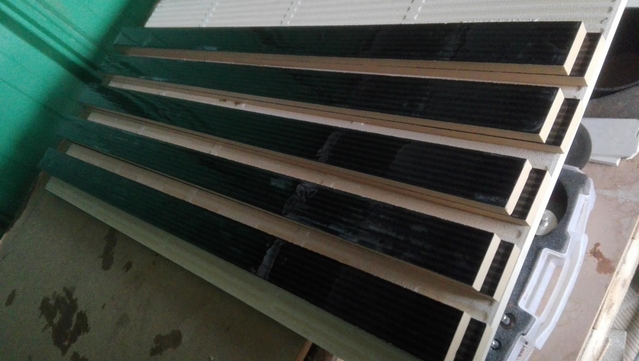 Paczka ciemnych, błyszczących płytek z jasnymi fugami, ułożonych warstwami w transporcie, widoczne ślady kleju na powierzchni.