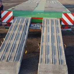 Zielony transportowy samochód ciężarowy z opuszczonymi rampami najazdowymi, widok z tyłu, tablica rejestracyjna widoczna.