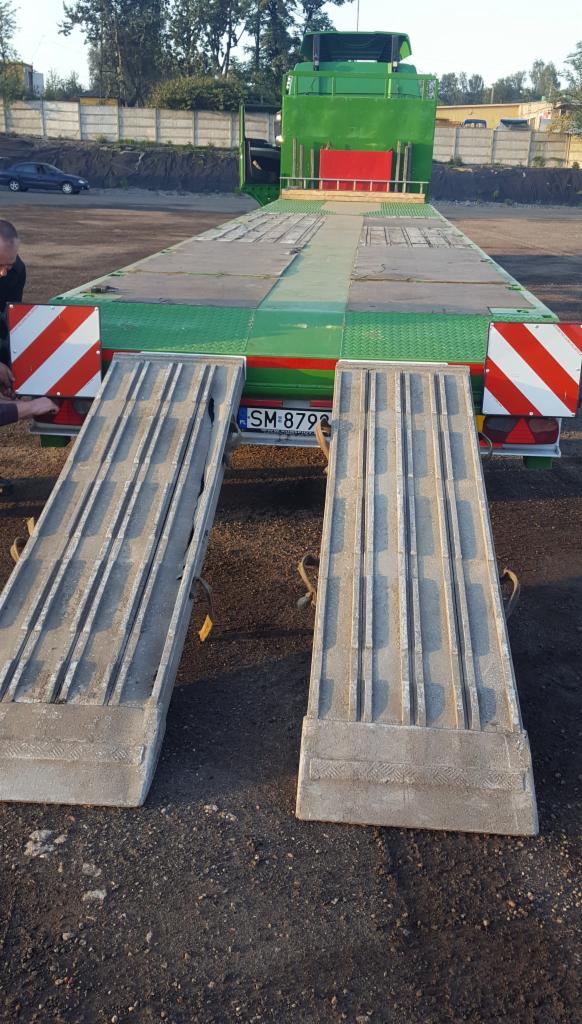 Zielony transportowy samochód ciężarowy z opuszczonymi rampami najazdowymi, widok z tyłu, tablica rejestracyjna widoczna.