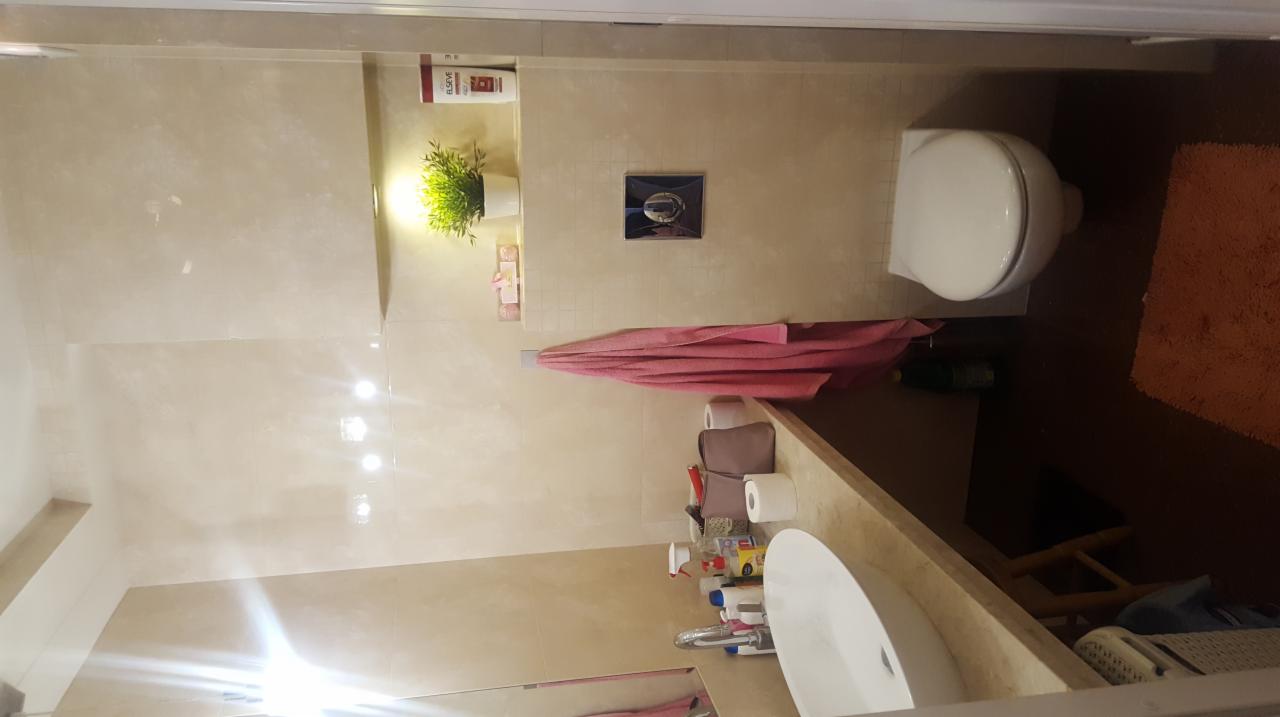 Umywalka, toaleta i beżowe płytki w wykończonej łazience, z widoczną armaturą i akcesoriami.