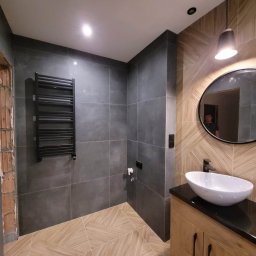 Dzik bud - Nowoczesna łazienka z szarymi płytkami ściennymi, drewnopodobną podłogą ułożoną we wzór jodełki, czarnym grzejnikiem drabinkowym i owalną umywalką nablatową na szafce z drewnianym frontem.