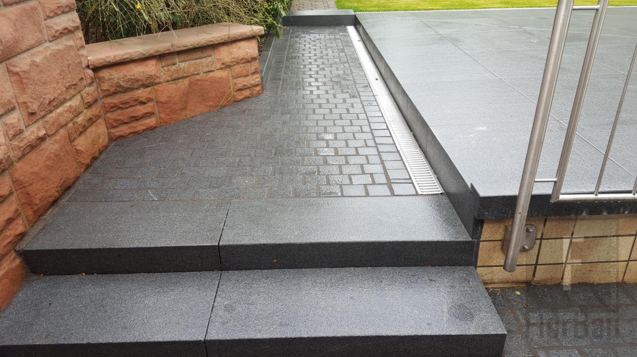 Granitowe schody prowadzące na taras wyłożony kamienną kostką, z odpływem liniowym i niskim murkiem z czerwonego piaskowca.