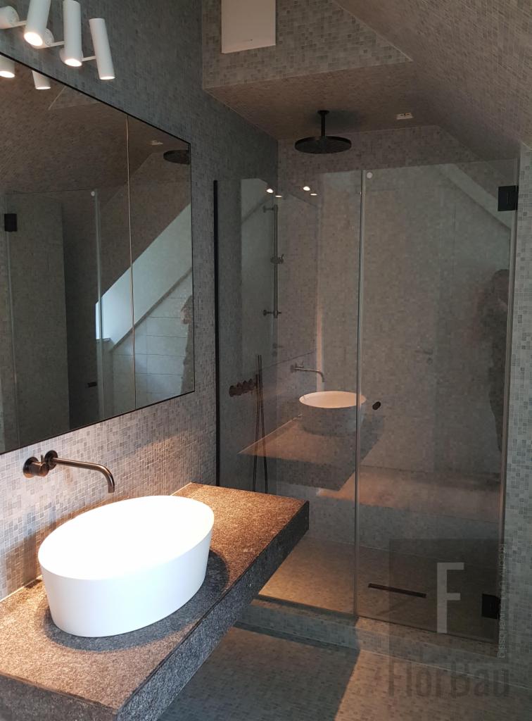 Nowoczesna łazienka z kabiną prysznicową typu walk-in, umywalką nablatową na blacie z ciemnego kamienia, mozaiką na ścianach i suficie oraz czarną armaturą.