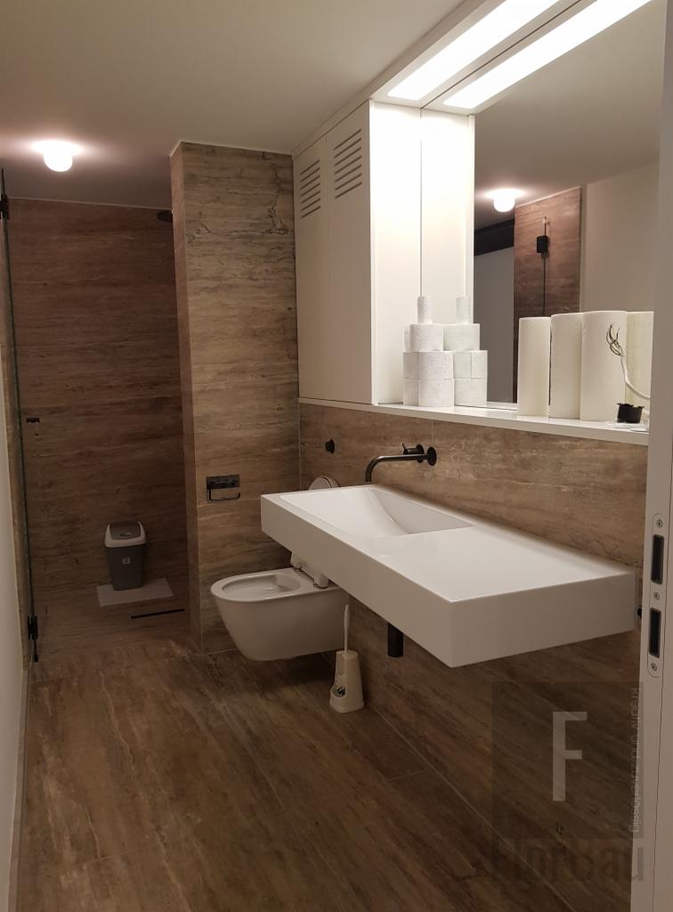 Nowoczesna łazienka z beżowymi płytkami imitującymi trawertyn, wisząca biała umywalka z czarną armaturą, podwieszana toaleta i szklana kabina prysznicowa.