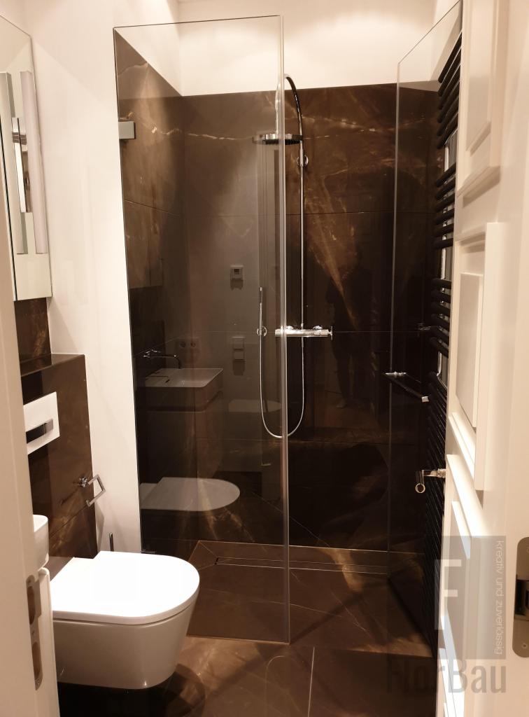 Nowoczesna łazienka z kabiną prysznicową typu walk-in, brązowe płytki imitujące marmur na ścianach i podłodze, biała toaleta wisząca i minimalistyczna umywalka.