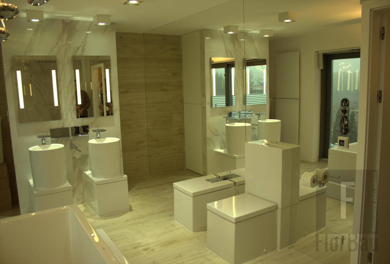 Nowoczesna łazienka z białymi, cylindrycznymi umywalkami i podwieszanymi toaletami, lustra z podświetleniem LED, płytki imitujące marmur na ścianach, jasna podłoga z płytek imitujących drewno...