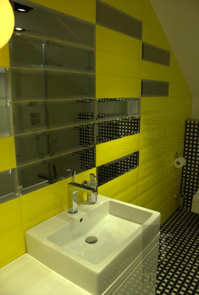 Żółto-szara łazienka z lustrzanymi płytkami, białą umywalką i czarno-białą podłogą w geometryczny wzór.