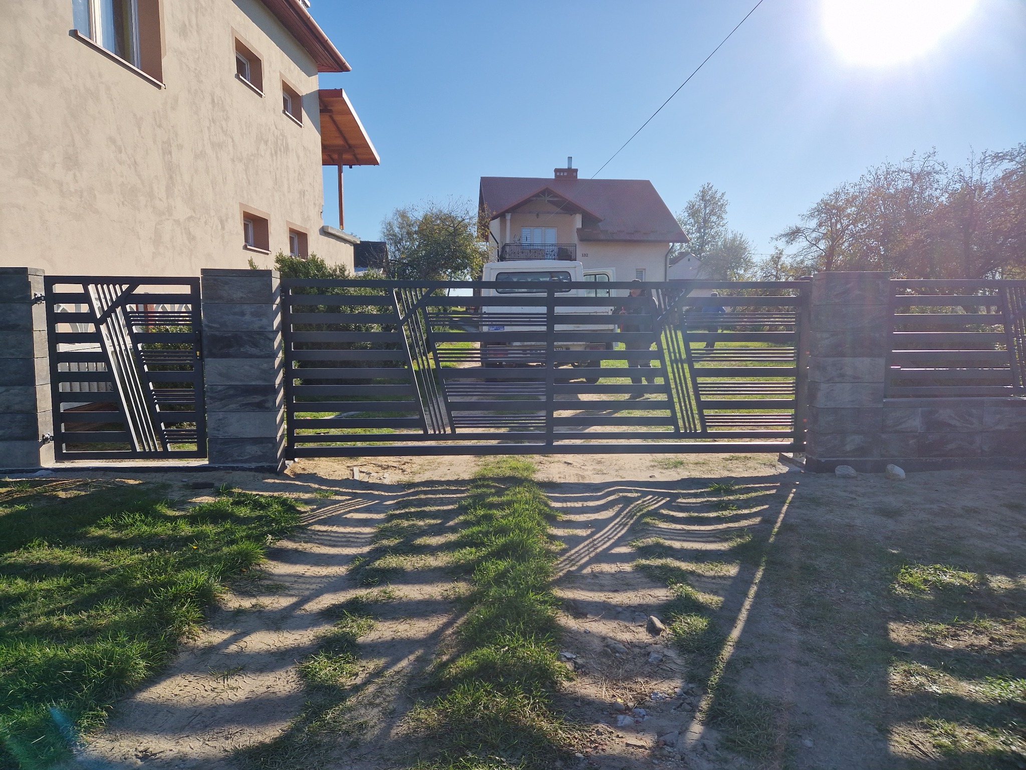 Nowoczesna brama wjazdowa z metalowymi przęsłami i kamiennymi słupkami w Głogowie Małopolskim, widok z zewnątrz posesji, w tle dom.