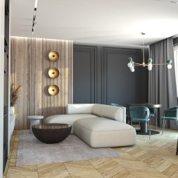 ODMIEŃ TO Martyna Raszka - Elegancki salon z narożną sofą, drewnianą ścianą z dekoracjami i parkietem w jodełkę. Nowoczesne oświetlenie i stonowana kolorystyka tworzą przytulną atmosferę.