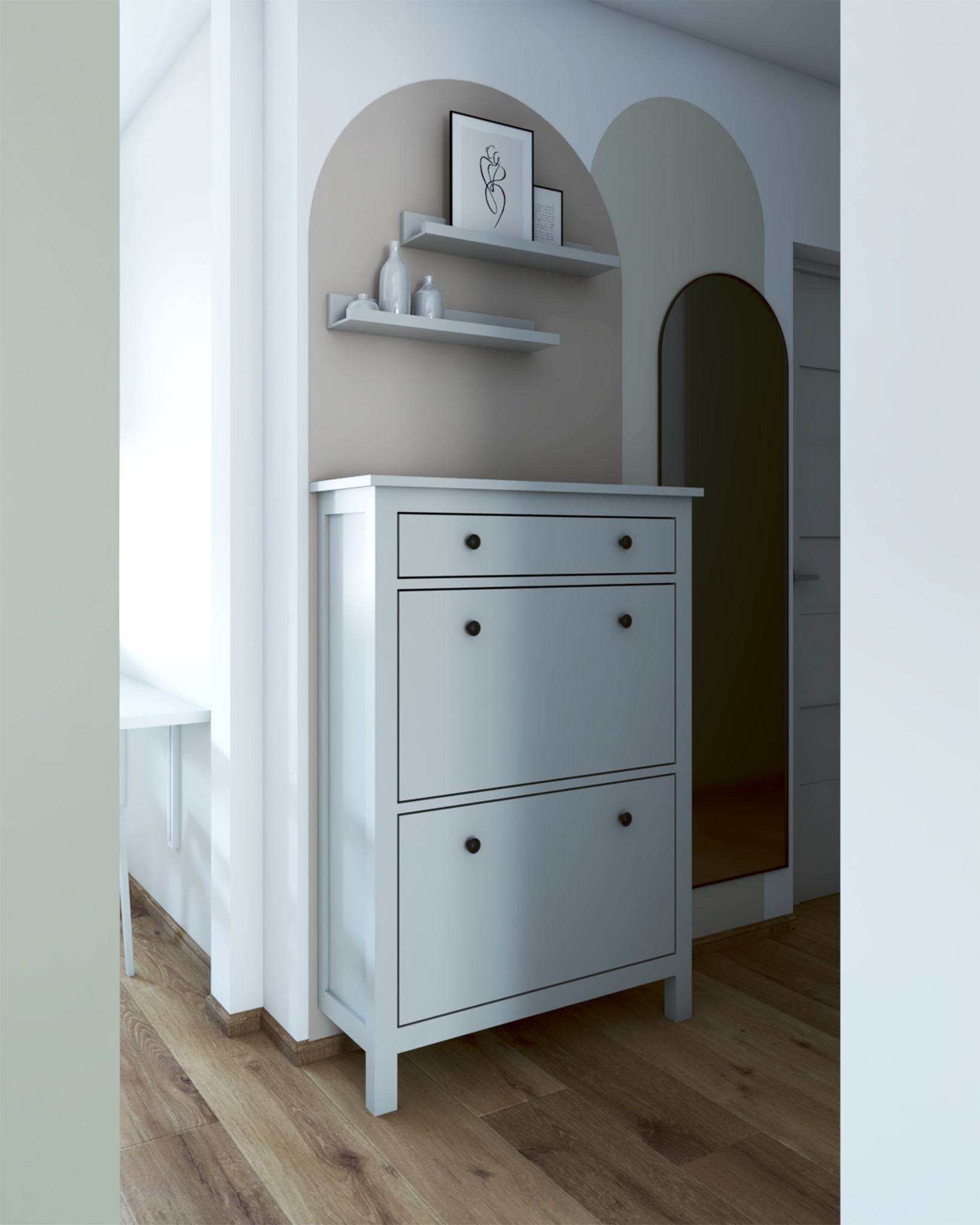 Biała szafka na buty z szufladą i półkami w przedpokoju. Nad nią półki z dekoracjami i grafika. Łukowe przejście do innego pomieszczenia. Drewniana podłoga.