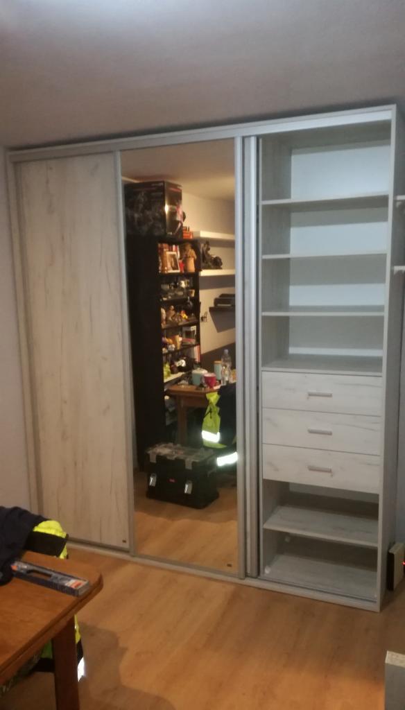 Szafa przesuwna z lustrem i otwartymi półkami, widoczne odbicie wnętrza pokoju z narzędziami i elementami garderoby.