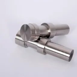 Dwa metalowe, cylindryczne elementy z kołnierzami leżące jeden na drugim na białym tle, widoczne ślady obróbki.