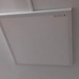 Kwadratowy panel LED zamontowany na białym suficie, widoczne delikatne oświetlenie.