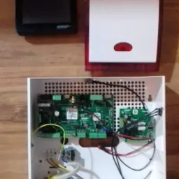 Centrala alarmowa z modułem sterującym i sygnalizatorem akustyczno-optycznym, widoczne wewnętrzne komponenty elektroniki i okablowanie.