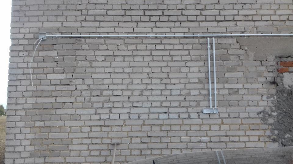 Szara ceglana ściana budynku z poprowadzonymi na zewnątrz rurami instalacji elektrycznej i puszkami przyłączeniowymi.