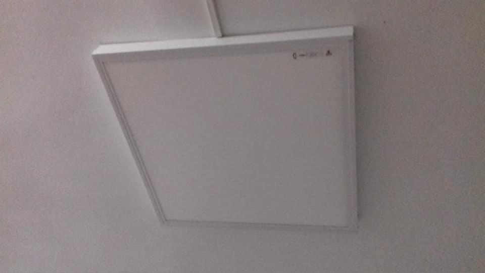 Kwadratowy panel LED zamontowany na białym suficie, widoczne delikatne oświetlenie.