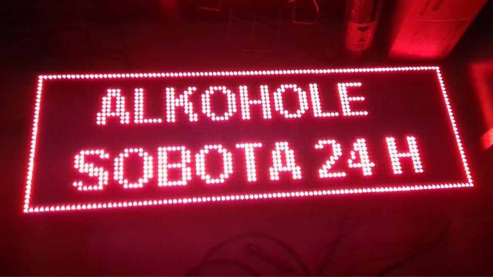 Podświetlany, czerwony szyld LED z napisem 'ALKOHOLE SOBOTA 24 H' w kropki, widoczny w ciemnym otoczeniu.