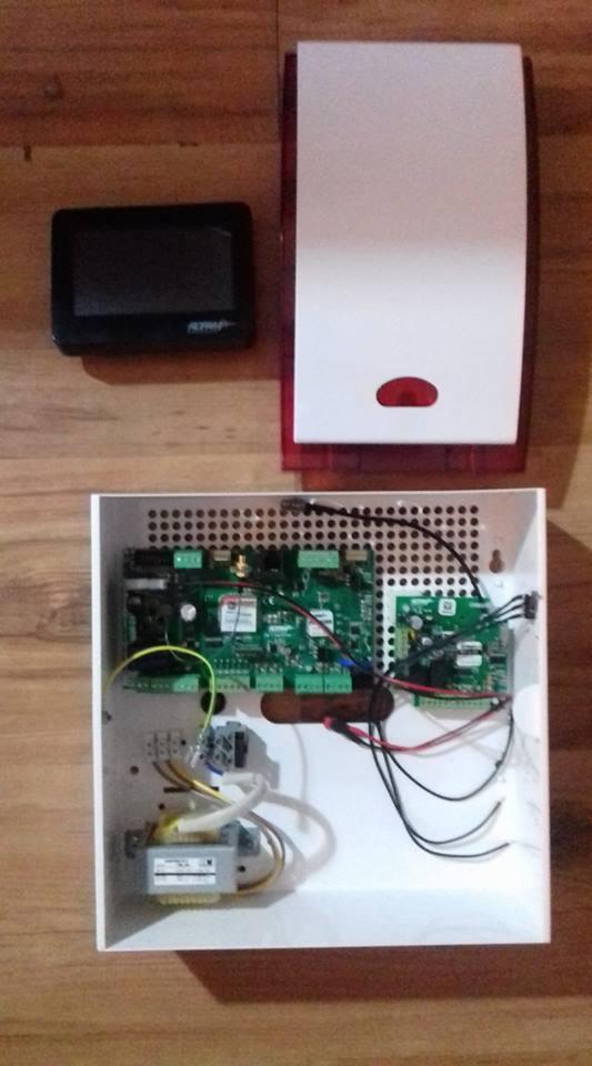 Centrala alarmowa z modułem sterującym i sygnalizatorem akustyczno-optycznym, widoczne wewnętrzne komponenty elektroniki i okablowanie.