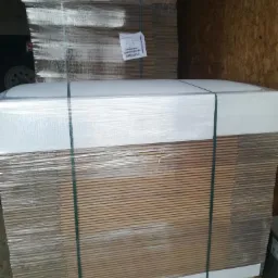 Paleta z zapakowanymi w folię i spiętymi taśmą kartonami oraz białymi płytami, widoczne ślady użytkowania palety.