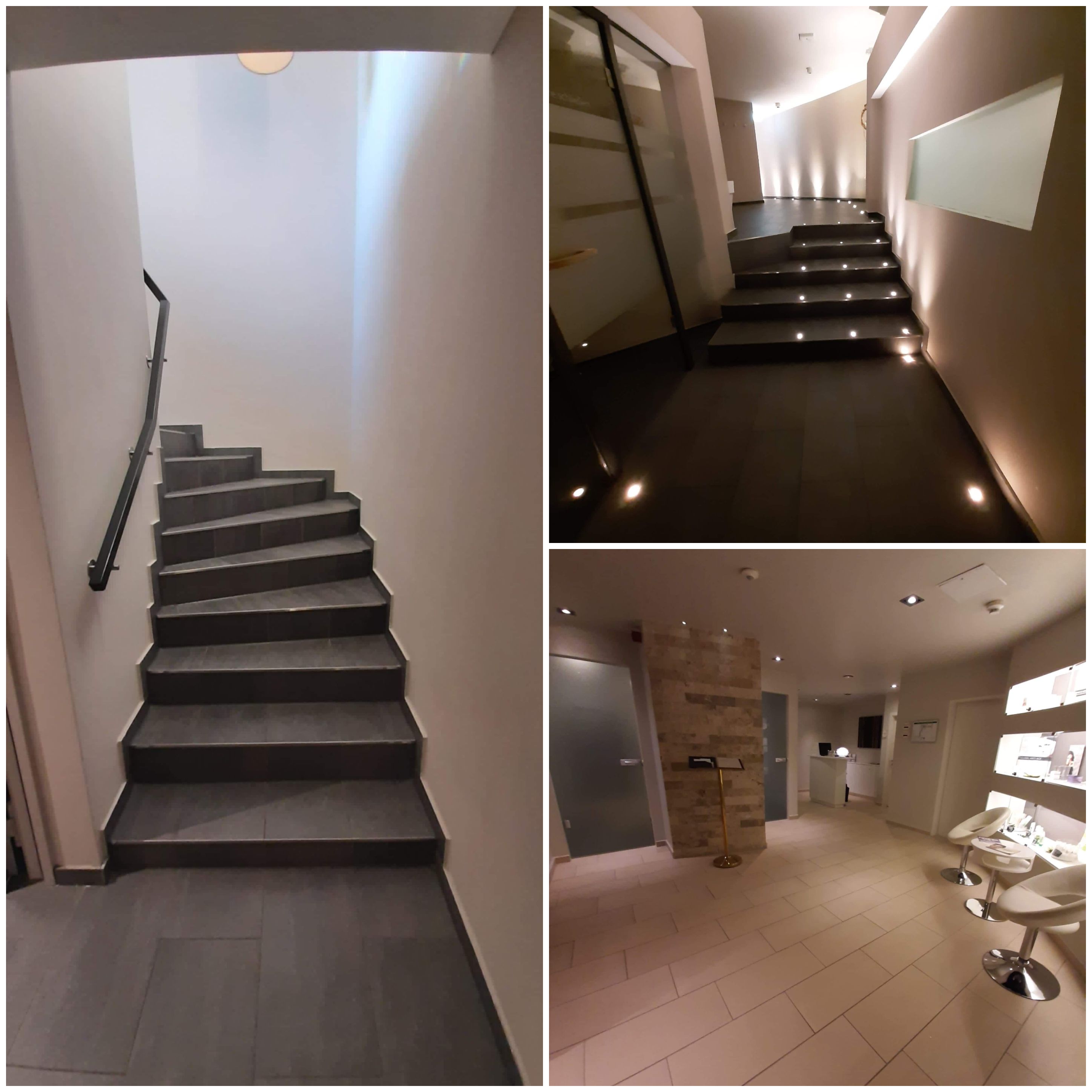 Klatka schodowa z szarymi płytkami, czarną poręczą i oświetleniem punktowym, widok na wykończone wnętrze z jasnymi płytkami podłogowymi i białymi krzesłami barowymi.