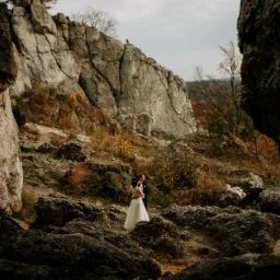 Para młoda w strojach ślubnych pozuje wśród wapiennych skał na tle jesiennego krajobrazu.