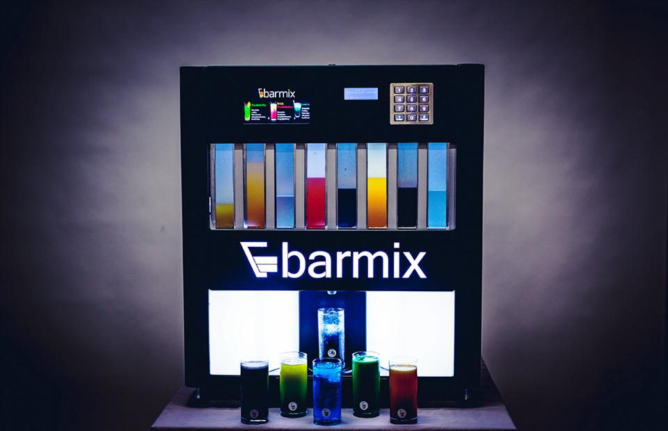 Automatyczny dystrybutor drinków Barmix z podświetlanym logo i rzędami kolorowych płynów, prezentujący gotowe koktajle w szklankach.