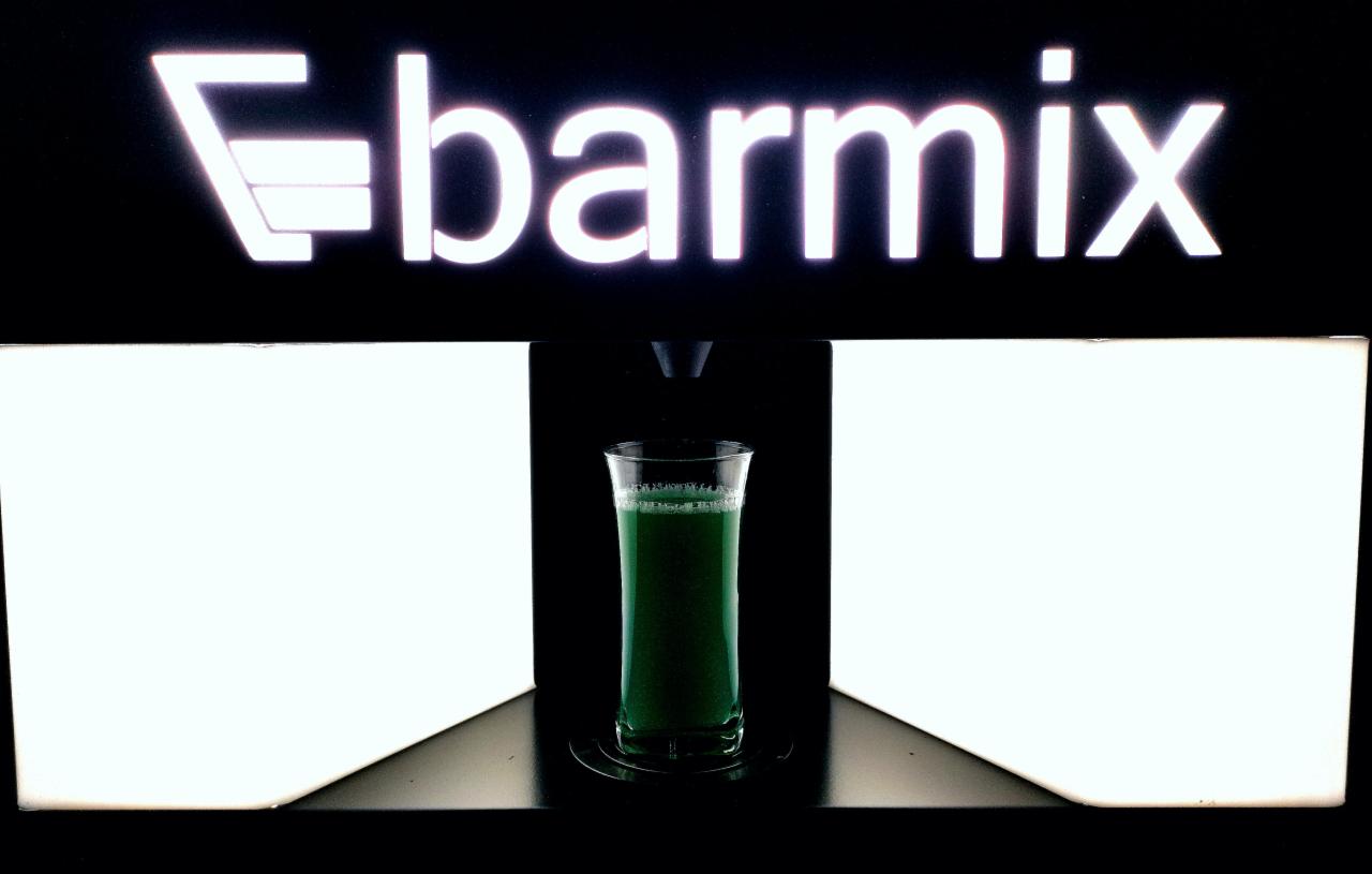 Szklanka zielonego soku lub koktajlu umieszczona w podświetlanej maszynie barmańskiej z logo 'barmix' na górze.