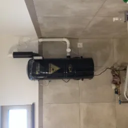 Centralny odkurzacz, model 'Black Edition', zamontowany w łazience z szarymi płytkami, widoczne rury i instalacja wodna.