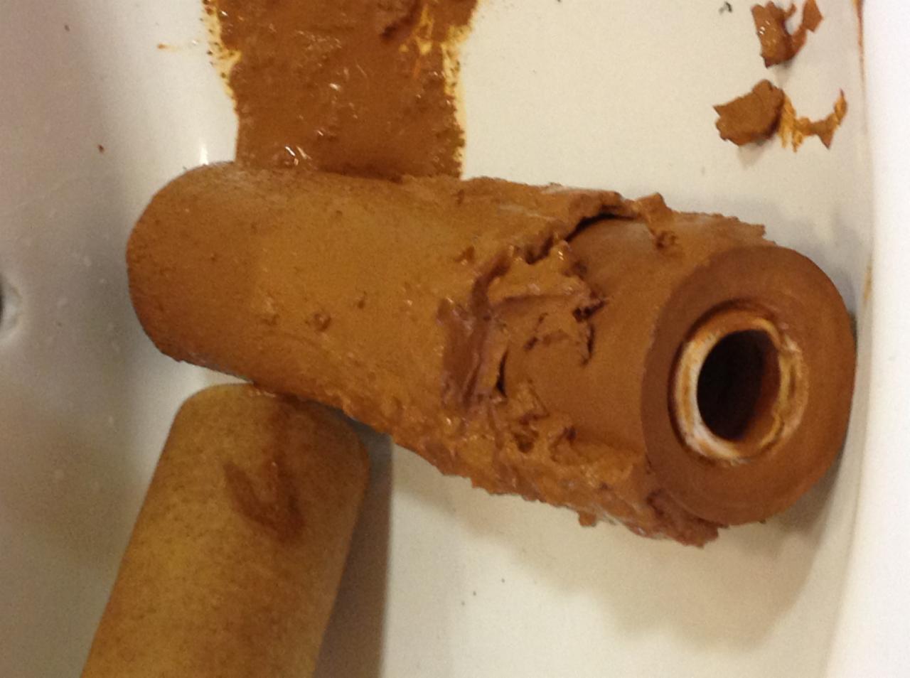 Zużyty, mocno zabrudzony brązowy filtr do wody leżący w białym zlewie, widoczne uszkodzenia struktury filtra.