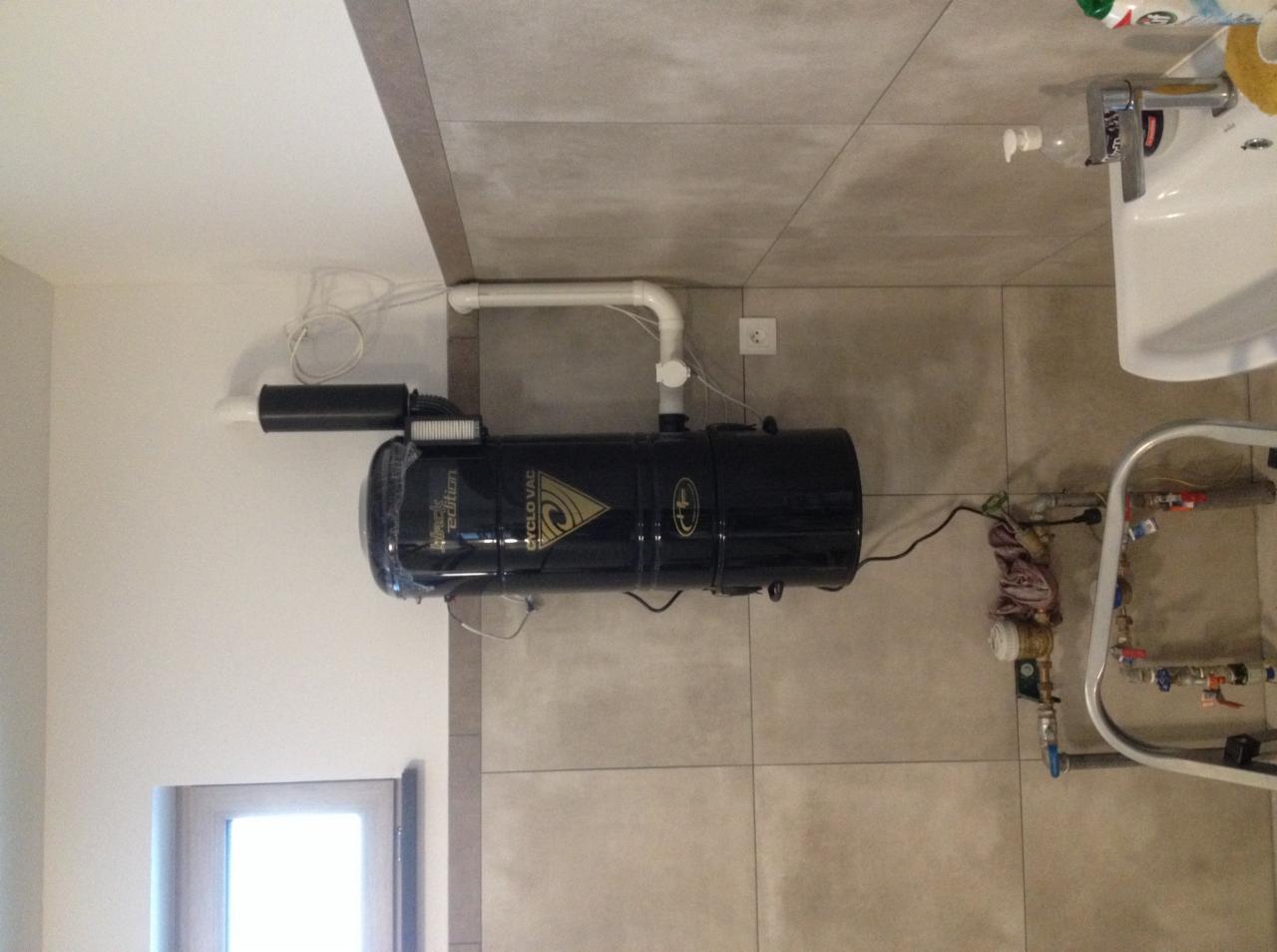 Centralny odkurzacz, model 'Black Edition', zamontowany w łazience z szarymi płytkami, widoczne rury i instalacja wodna.