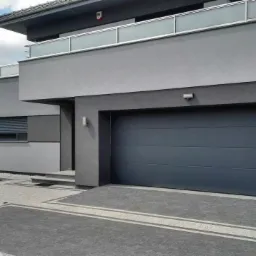 Nowoczesny dom jednorodzinny z szarą, segmentową bramą garażową i starannie ułożoną kostką brukową na podjeździe.