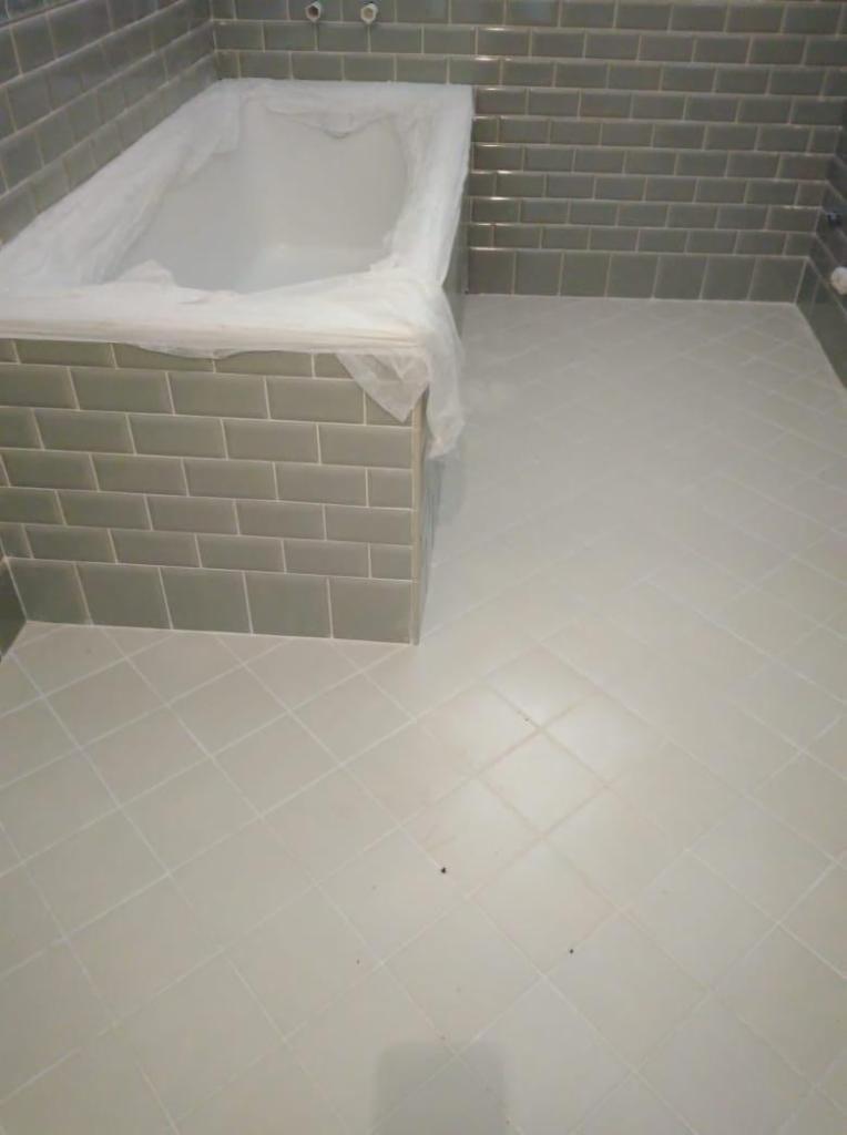 Łazienka w trakcie prac wykończeniowych: ściany wyłożone szarą cegiełką, podłoga wyłożona jasnymi kwadratowymi płytkami ułożonymi pod kątem, wanna zabezpieczona folią ochronną.