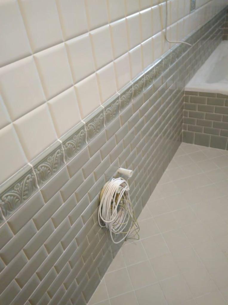 Wykończona łazienka z białymi i szarymi płytkami, dekoracyjnym pasem z ornamentem i zwisającym kablem elektrycznym.