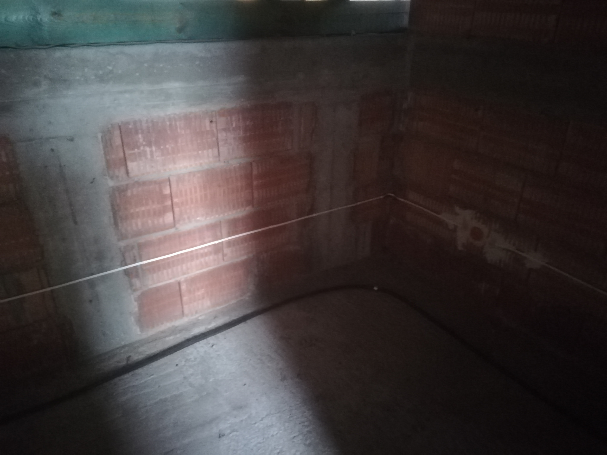 Surowe wnętrze z ceglanymi ścianami w trakcie prac instalacyjnych, widoczny przewód elektryczny i napięta linka wyznaczająca poziom.