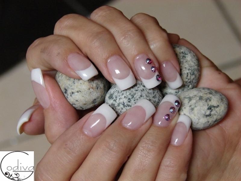 Dłonie z białym manicure francuskim i zdobieniami z cyrkonii, trzymające szare kamienie.