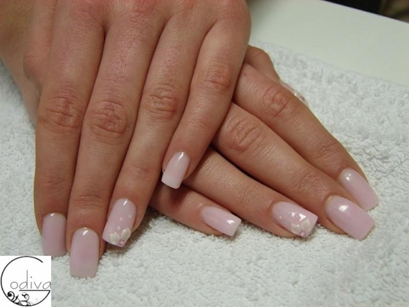 Dłonie z delikatnym, jasnoróżowym manicure hybrydowym, zdobionym małymi, białymi kwiatkami na jednym paznokciu, ułożone na białym ręczniku frotte.