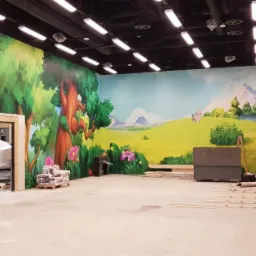 Malowidło ścienne z motywem leśnym i górskim w nowo wykończonym pomieszczeniu, widoczne materiały budowlane i worki z zaprawą.