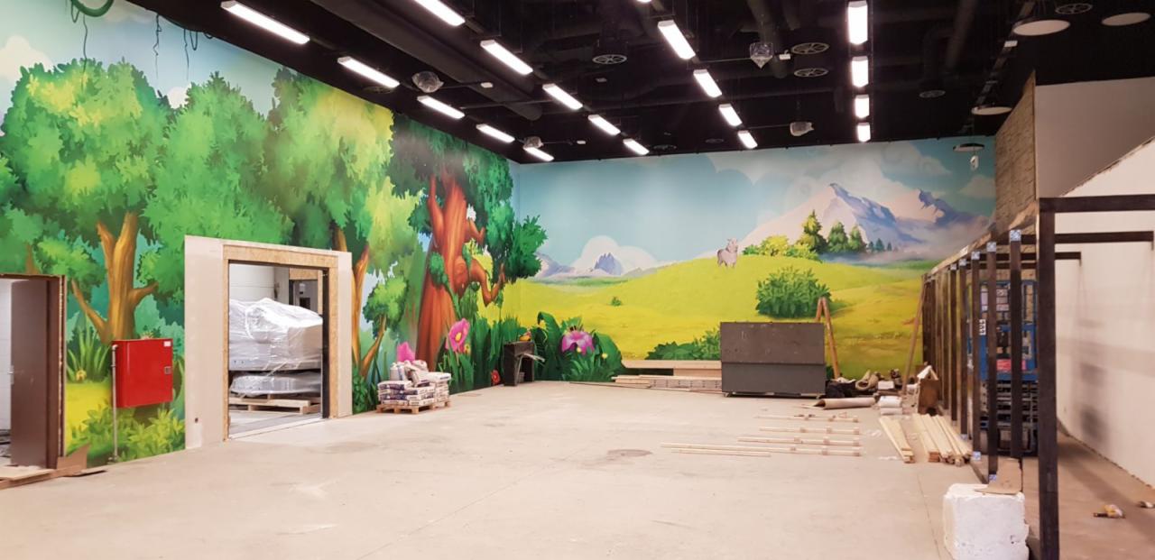 Malowidło ścienne z motywem leśnym i górskim w nowo wykończonym pomieszczeniu, widoczne materiały budowlane i worki z zaprawą.