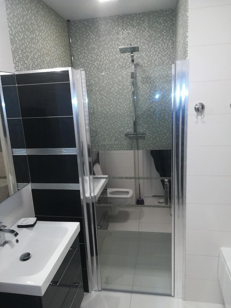 Nowoczesna łazienka z kabiną prysznicową typu walk-in, umywalką nablatową na czarnej szafce i mozaiką na ścianie w strefie prysznica.