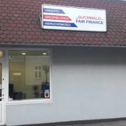 Fasada budynku firmy oferującej usługi finansowe, z widocznym szyldem 'Kredyty, Ubezpieczenia, Nieruchomości' oraz logo 'Buchwald Fair Finance'. W oknie widoczne rośliny doniczkowe i wnętrze biura.