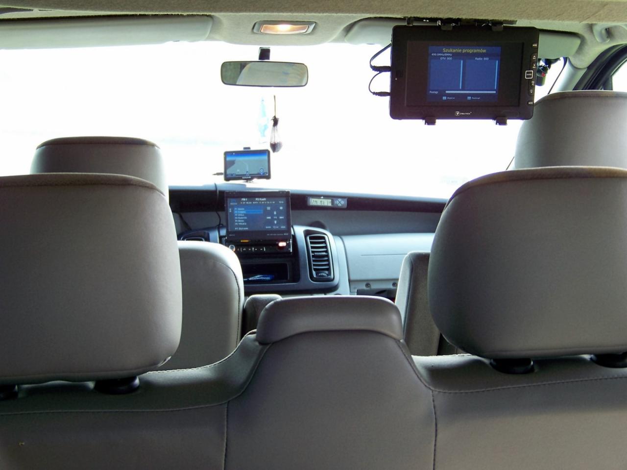 Wnętrze busa z widokiem na zamontowane ekrany: jeden pod sufitem z funkcją szukania programów i dwa mniejsze na desce rozdzielczej, widok z tylnych siedzeń.