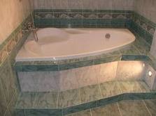 Wanna asymetryczna w obudowie z płytek ceramicznych, z podświetleniem LED, w łazience wykończonej w odcieniach zieleni i beżu.