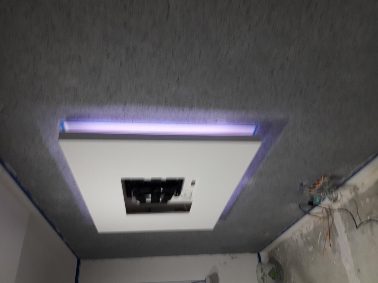 Szpachlowany sufit z wnęką oświetleniową i otworem na lampę, widoczne kable instalacji elektrycznej na ścianie, zabezpieczone taśmą malarską narożniki.