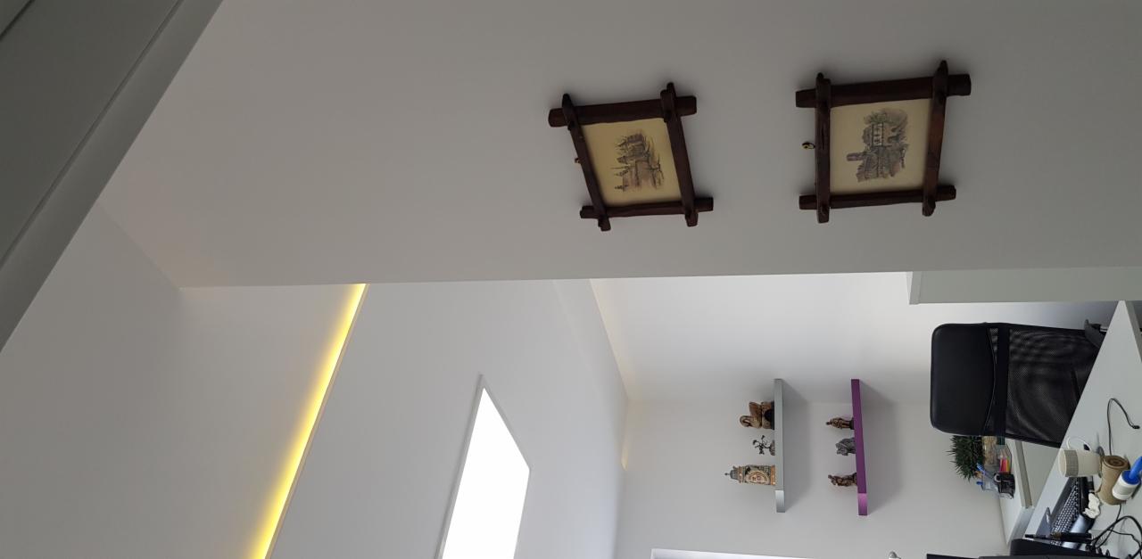Białe ściany i sufit z dwoma obrazkami w drewnianych ramkach, podświetlenie LED w rogu ściany, półki z dekoracjami, widok z dołu.