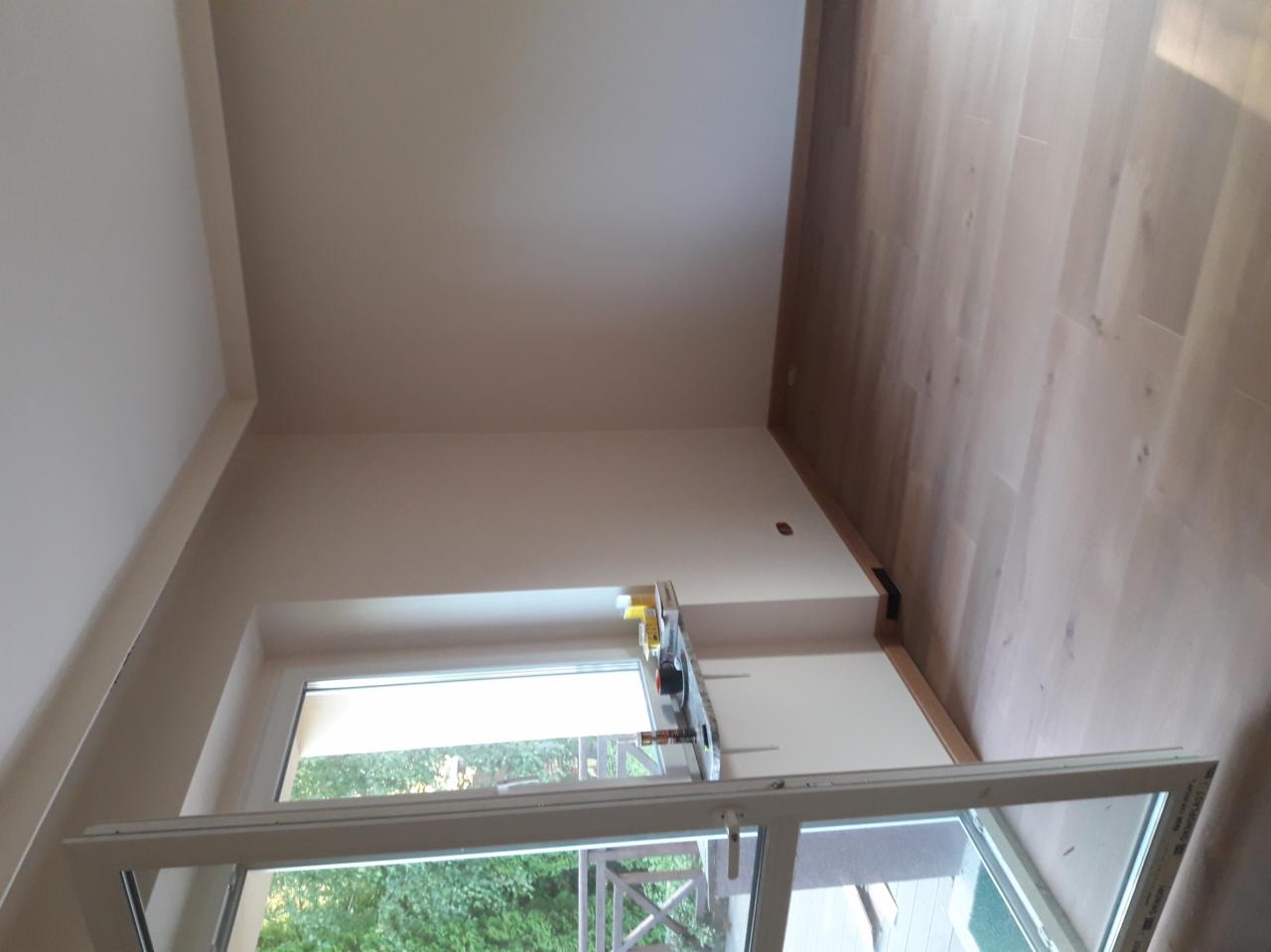 Jasne panele podłogowe w nowym pokoju z otwartym oknem, widok na zieleń i narzędzia na parapecie.