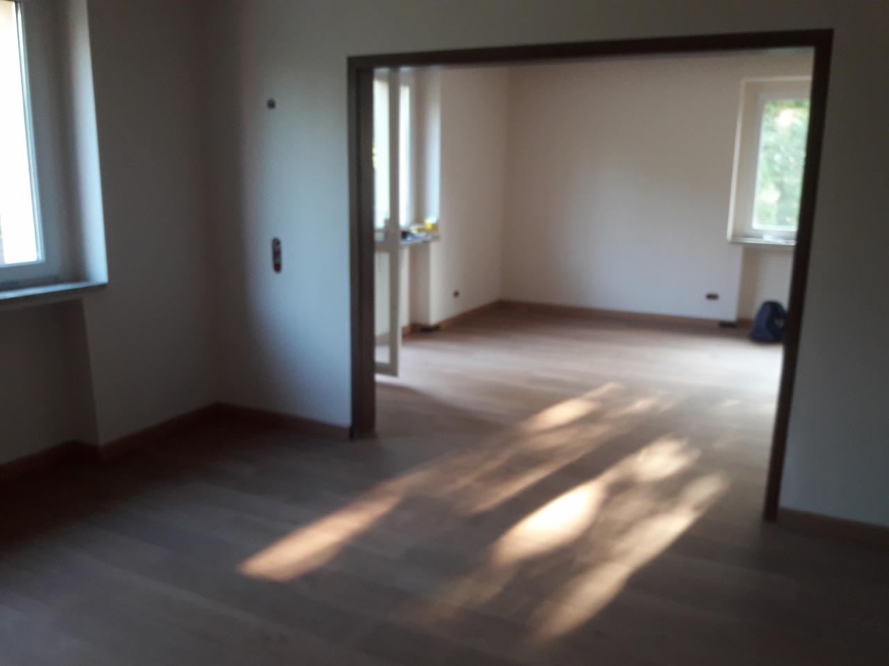 Jasne panele podłogowe w pustym pokoju z białymi ścianami, widoczne przez drewniane futryny drzwi, wpadające promienie słońca